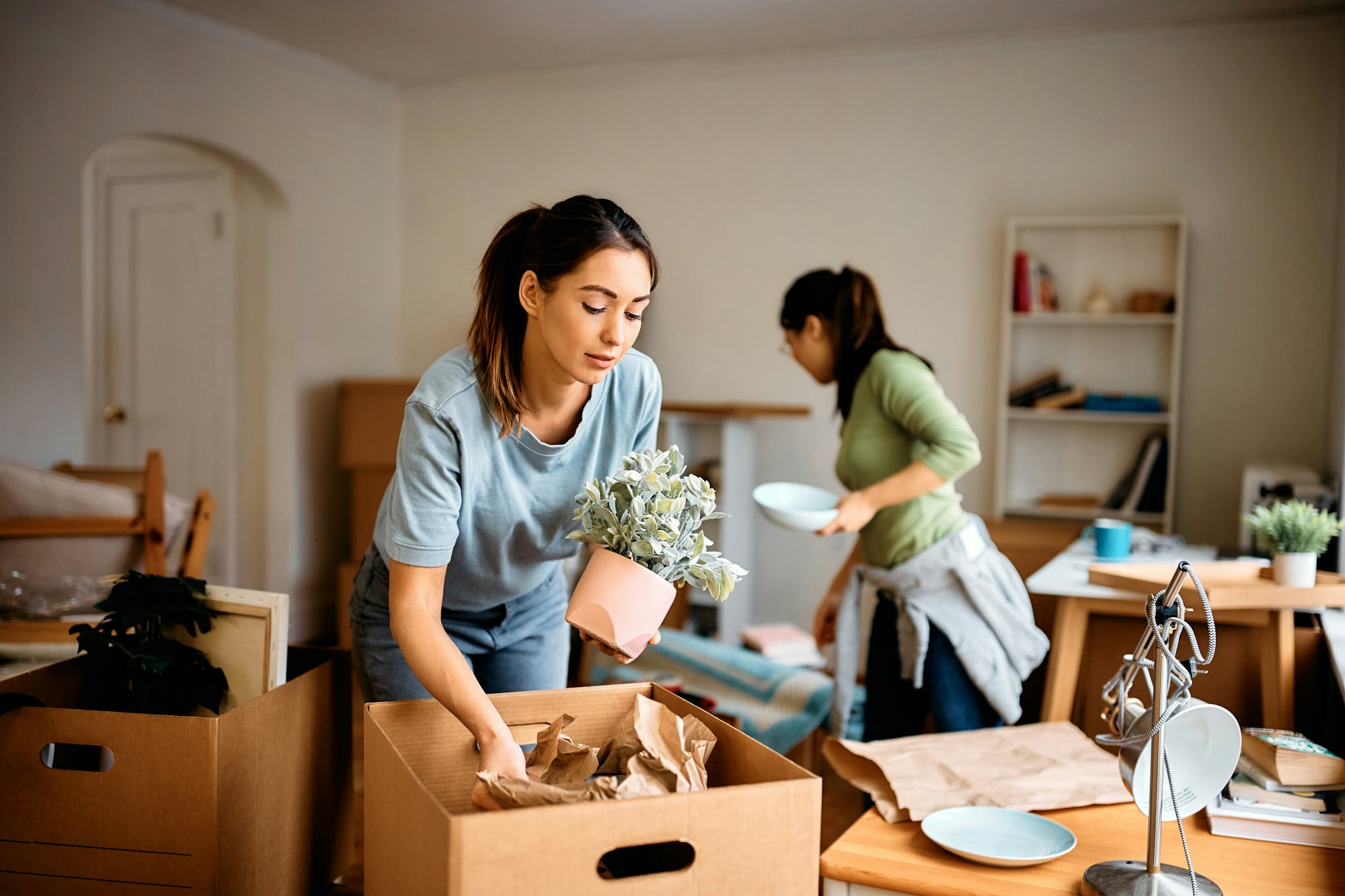Young woman and her friend packing their belongings while preparing to move out of the apartment.